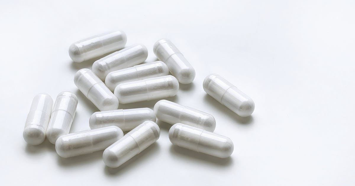 A pile of white capsule pills on a white background. 