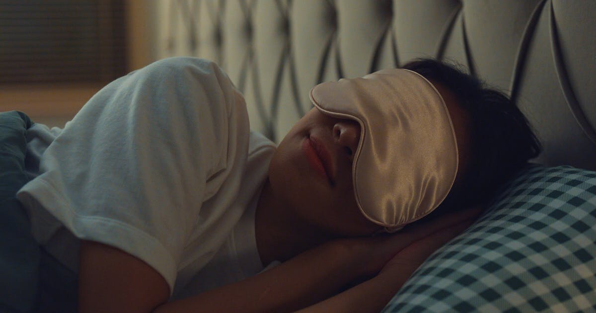 Woman lying on a bed, wearing an eye mask.