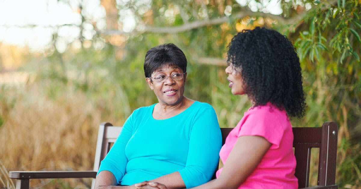 Two Black women sit on a bench.