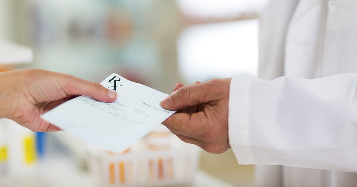 Close-up of two hands, one handing a prescription paper reading "RX" to the other.