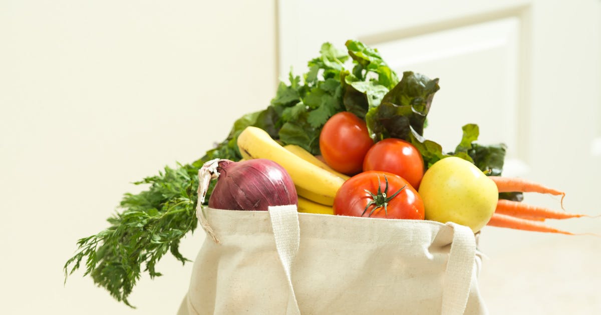 A cloth grocery bag overflowing with vegetables.