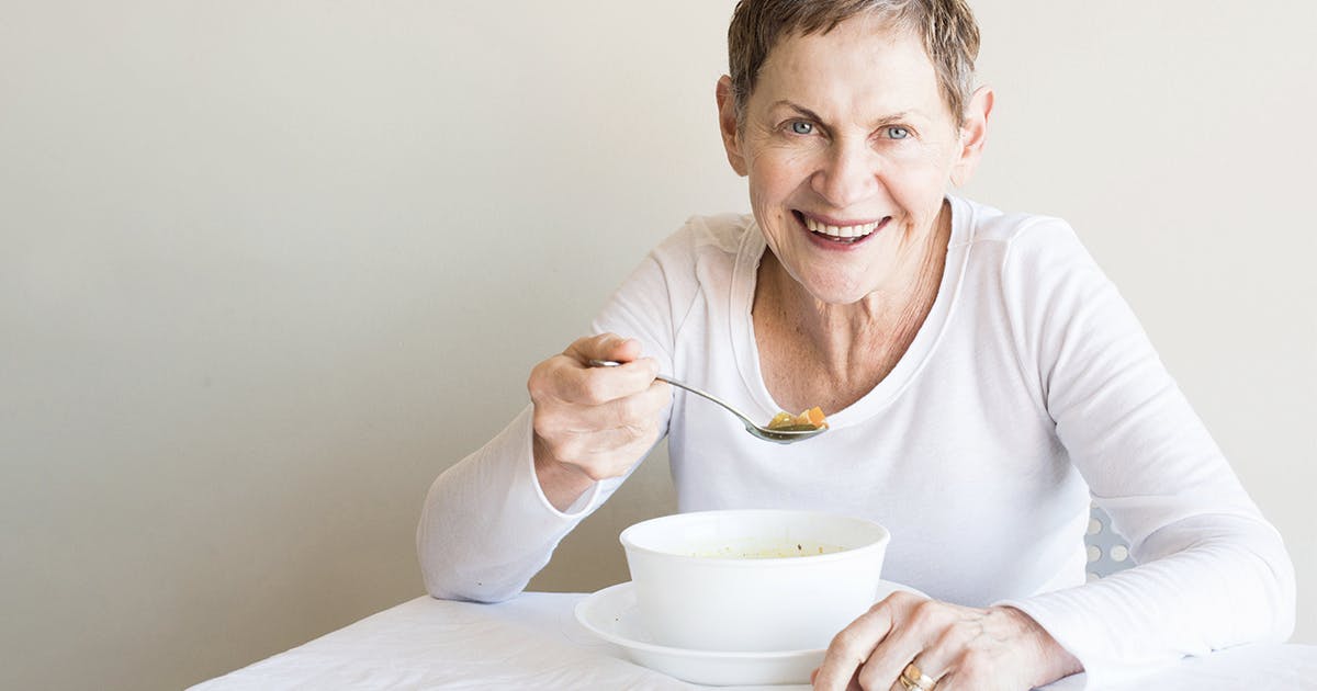 An older woman sits at a table eating.