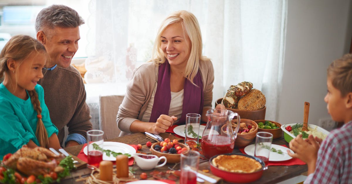 A happy man, woman, girl and boy sit at a table laden with Thanksgiving food. 