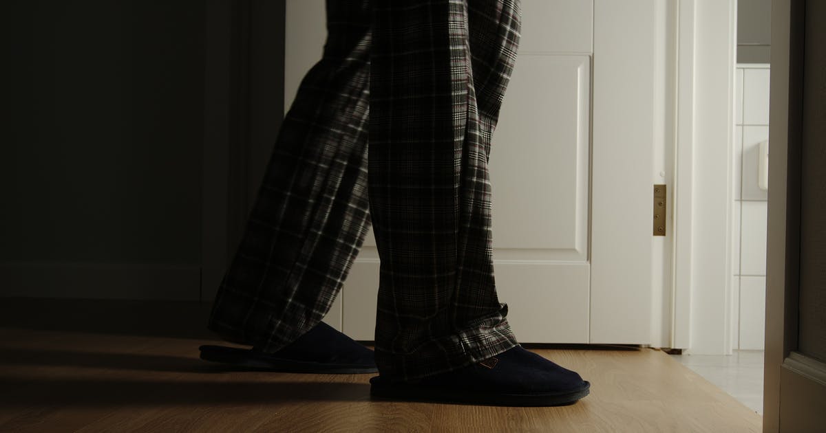 A pair of pajama- and slipper-clad legs enter a bathroom at night.