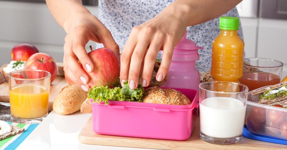  A woman packing a healthy lunch with an apple and sandwich.