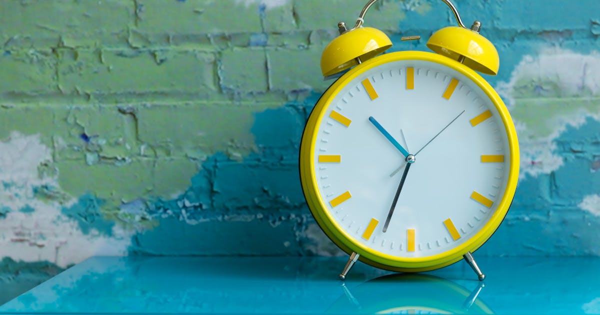 A bright yellow analog alarm clock on a table.