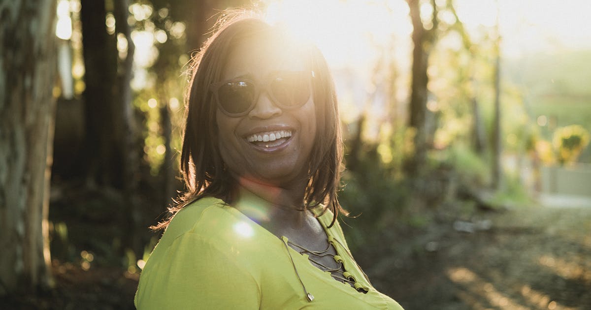 A smiling woman wearing sunglasses outdoors.