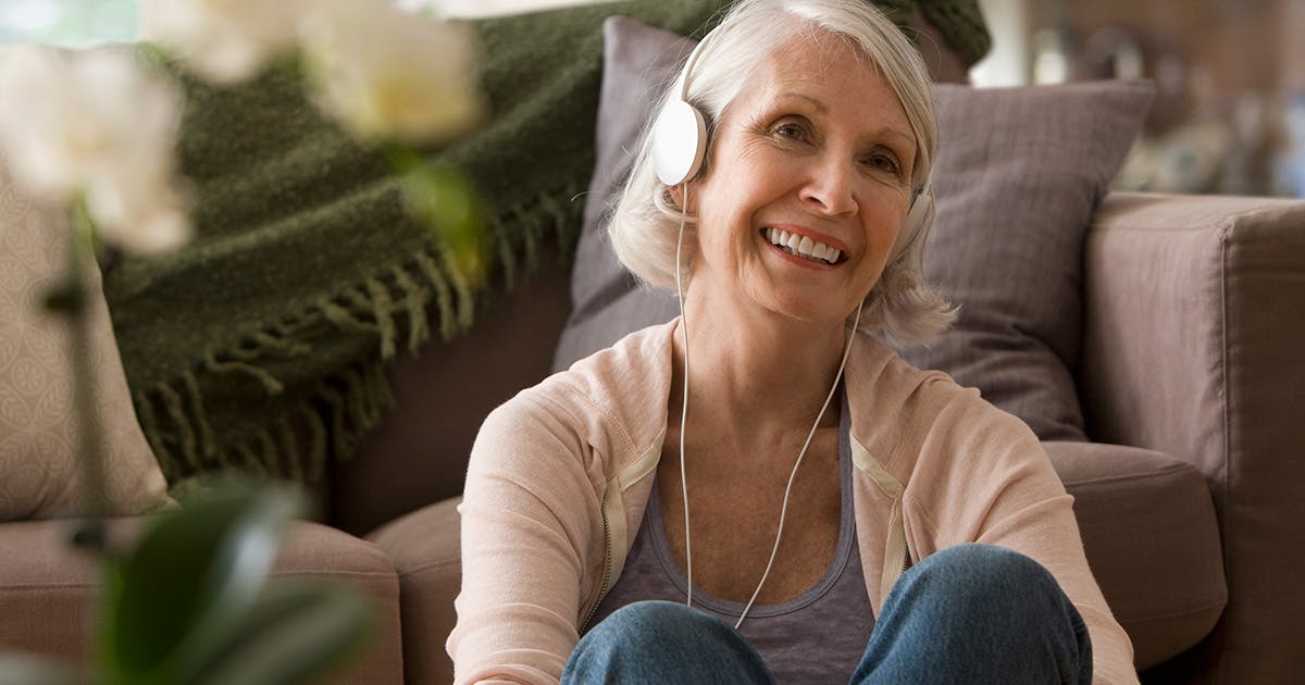 A smiling woman sitting on the floor in a living room with headphones on.