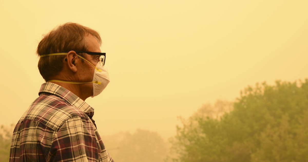 A man in a face mask stands outside on a smoky day.