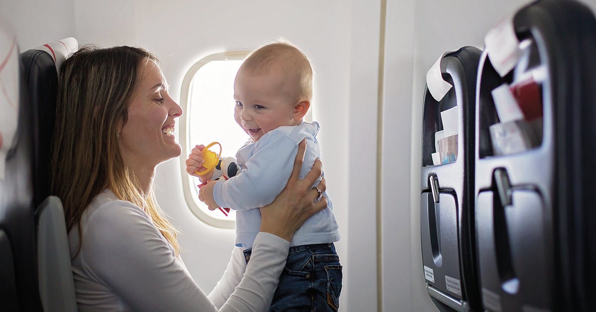 A mom holding a baby while seated on an airplane.
