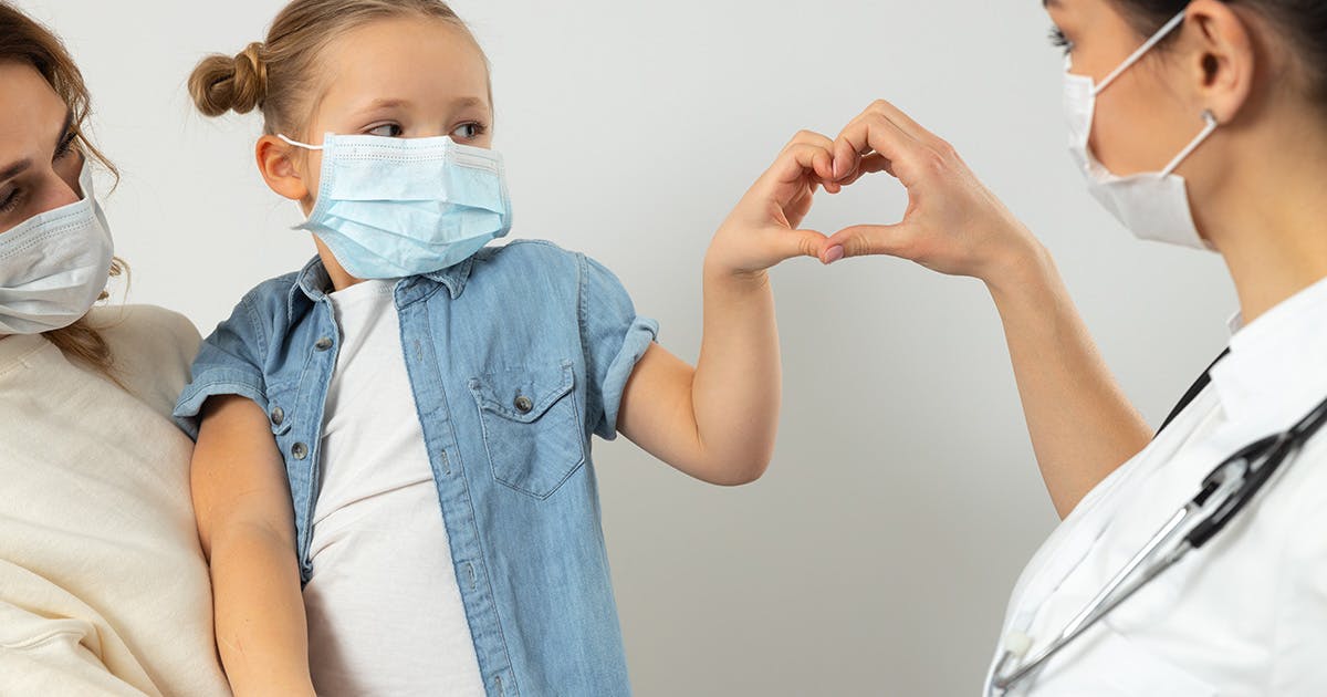 A child and a healthcare provider hold their hands together in the shape of a heart. 