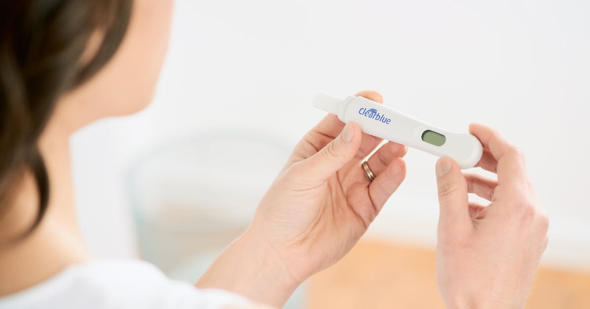 A woman, seen from behind, holds a pregnancy test in both hands.