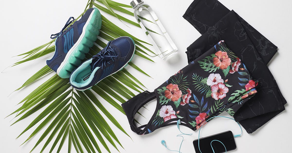 A collection of fitness-related items on a white background with an accent fern. Blue and teal sneakers, a water bottle, a floral print tank top, exercise pants, and a smartphone with blue earbuds. 