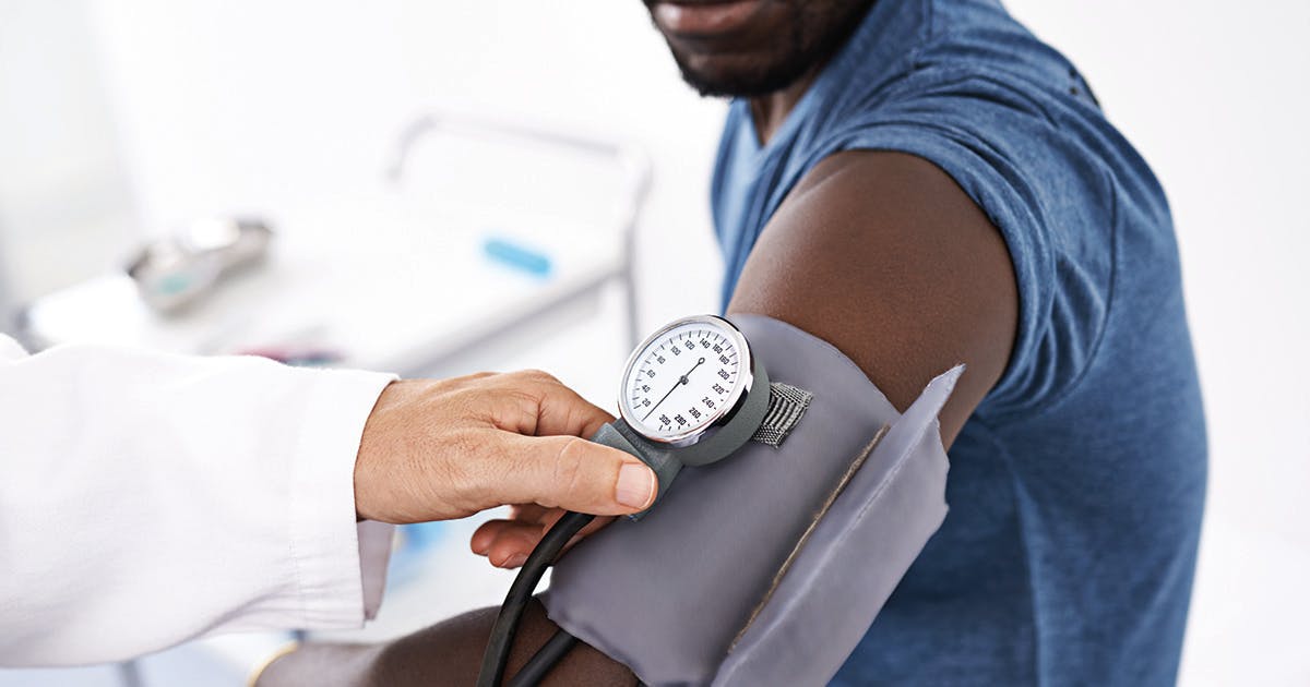 Close-up of a blood pressure cuff on a patient's arm with a provider's hand nearby. 