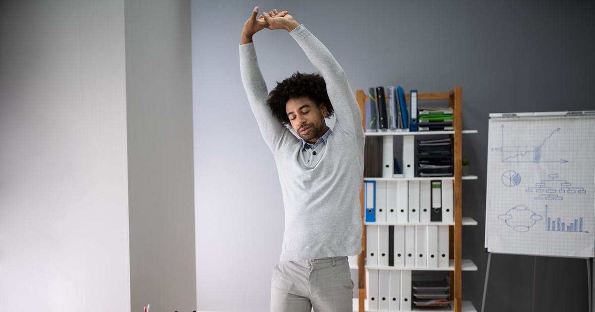 Man standing by his desk and stretching his arms above his head.