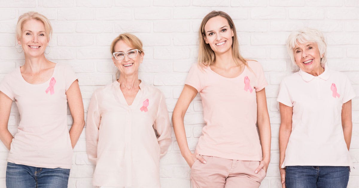 A row of smiling women wearing pink ribbons on their shirts