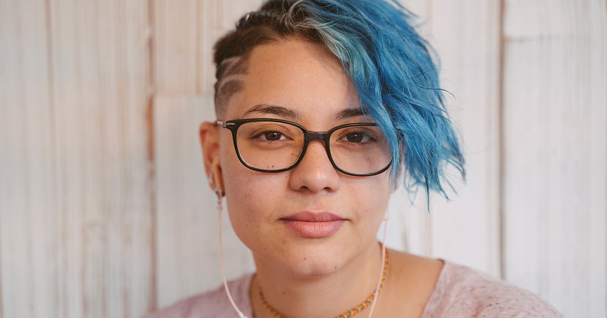 A teenager with blue hair and glasses.