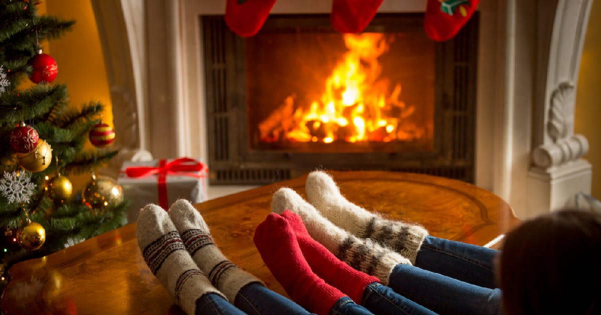 Three pairs of feet in warm, wool socks propped on a table near a fireplace.