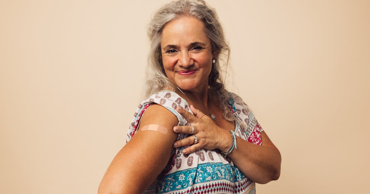 A smiling woman shows her flu vaccine bandage