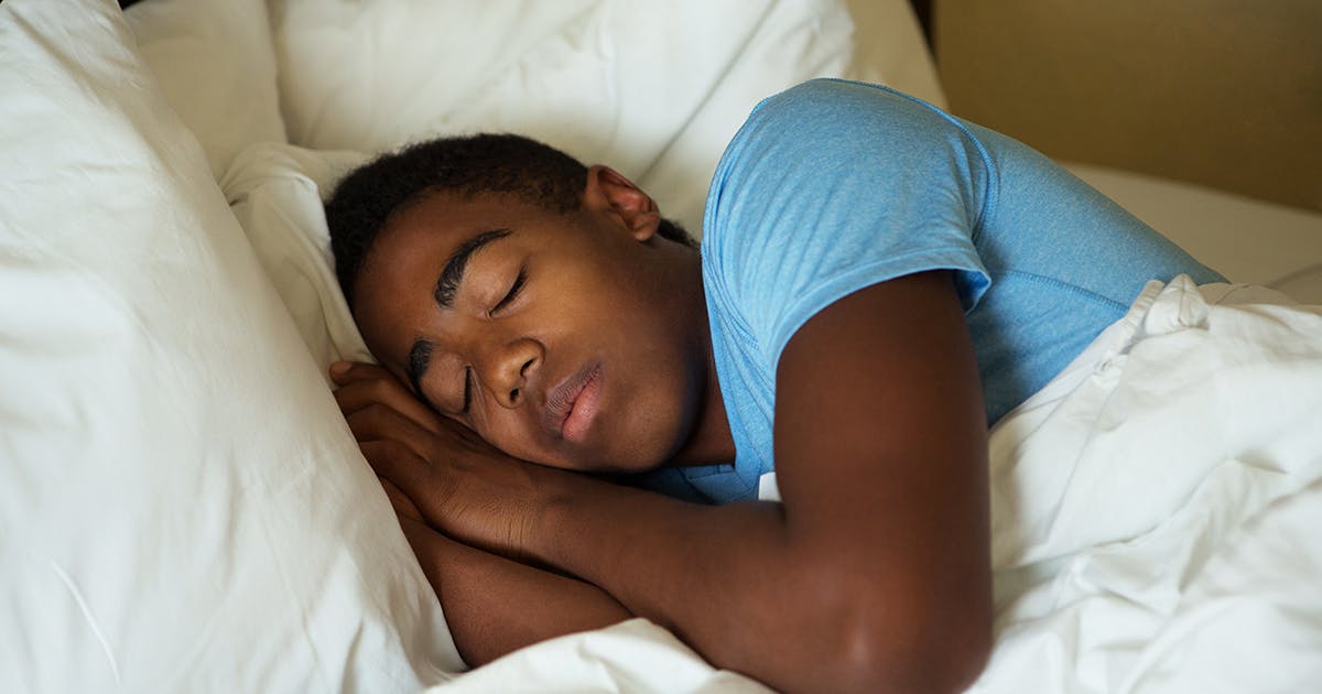 A teenage boy is sleeping in bed.