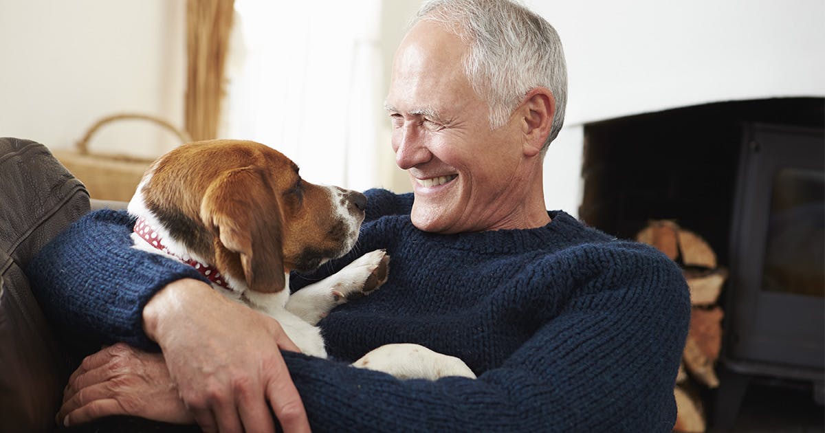 Smiling man cuddling with pet dog in a home setting.