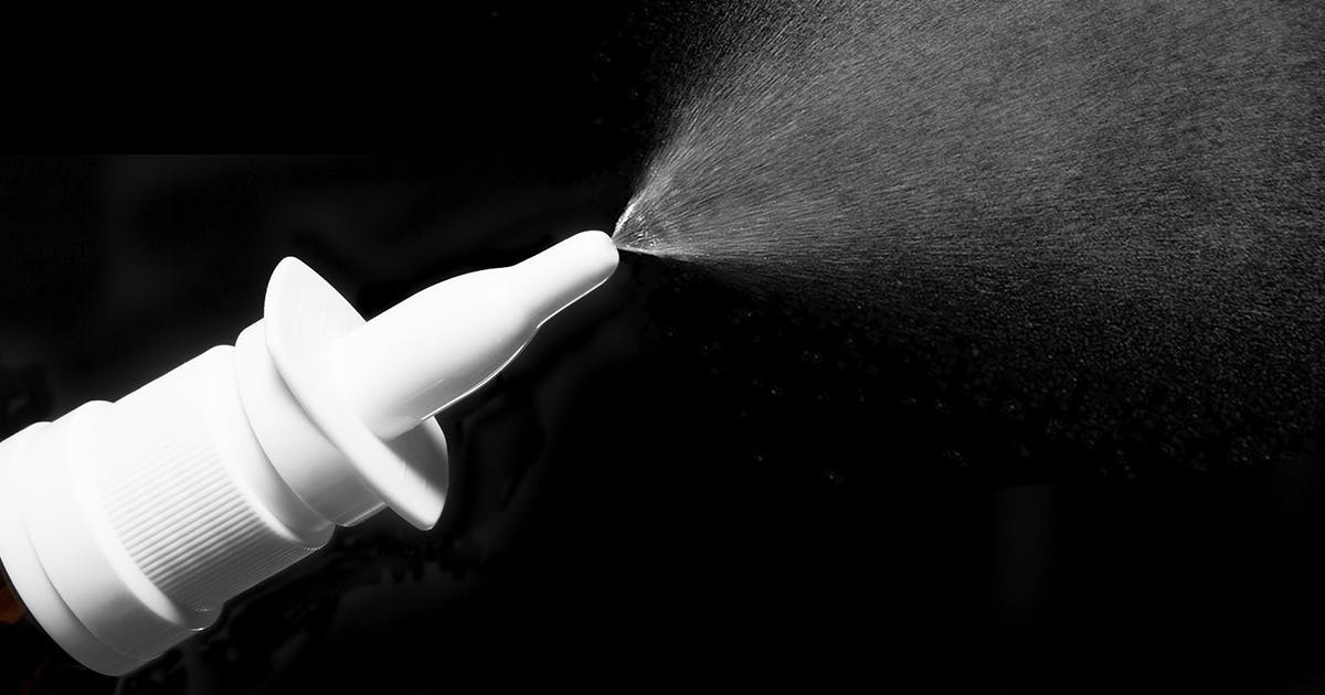 Close-up of a nasal spray bottle spraying liquid. 