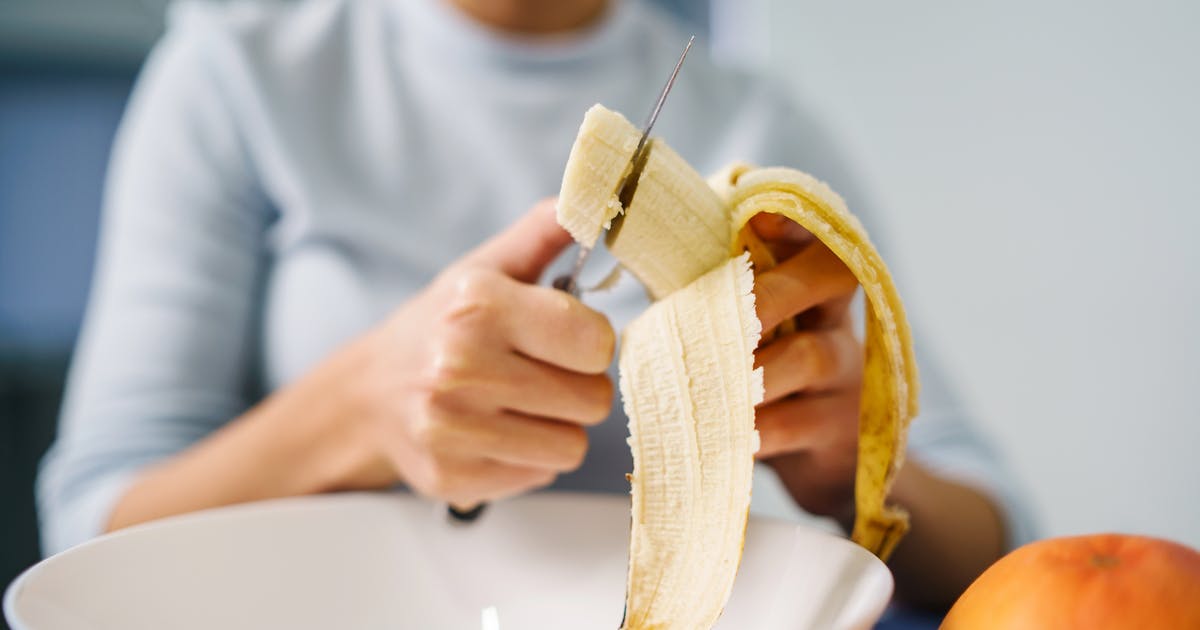 Hands slice a banana into a bowl