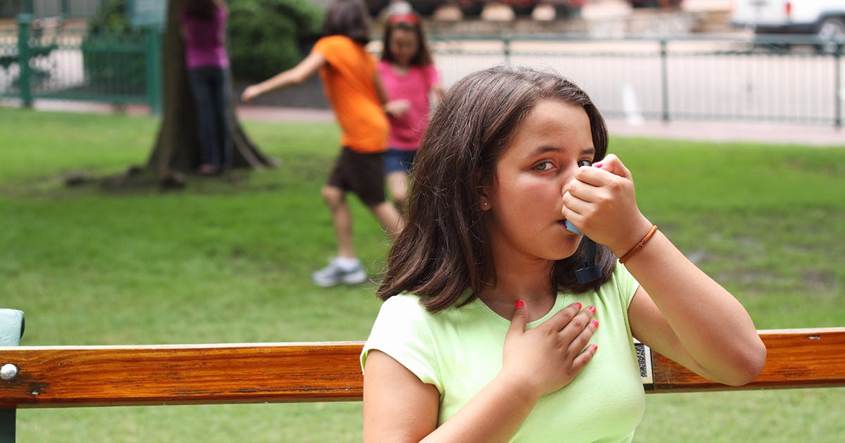 A girl uses an inhaler outdoors.